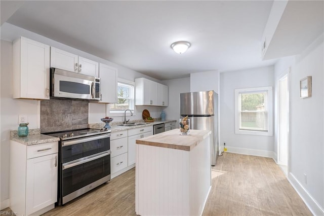 kitchen with stainless steel appliances, a sink, wood counters, white cabinets, and light wood-style floors