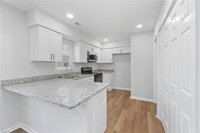 kitchen featuring light stone counters, stainless steel appliances, light wood-style floors, a sink, and a peninsula