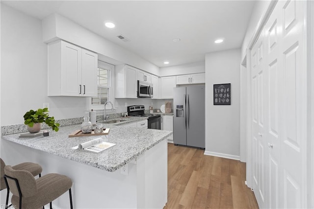 kitchen featuring appliances with stainless steel finishes, a kitchen breakfast bar, a peninsula, white cabinetry, and a sink