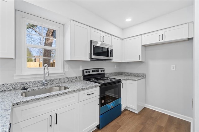 kitchen featuring white cabinets, electric range oven, stainless steel microwave, light stone countertops, and a sink