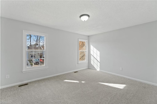 carpeted spare room with plenty of natural light, baseboards, and a textured ceiling