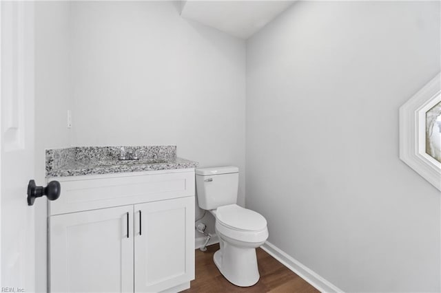 half bath featuring toilet, baseboards, wood finished floors, and vanity