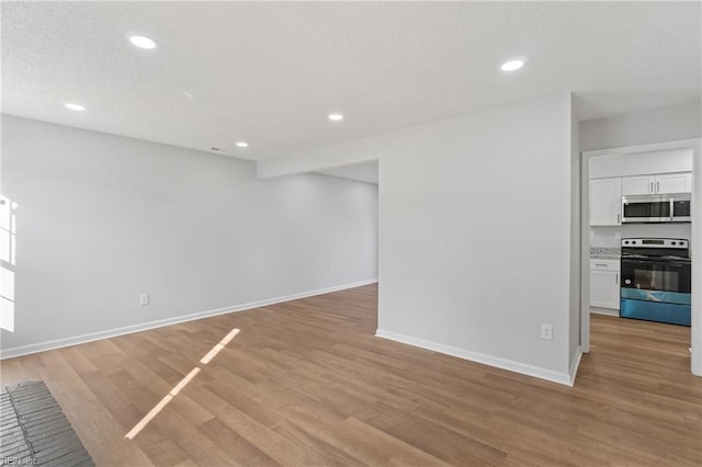 unfurnished living room featuring light wood-style flooring, baseboards, a textured ceiling, and recessed lighting