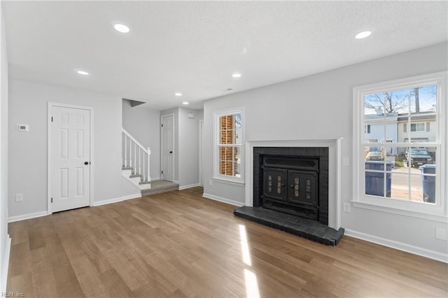 unfurnished living room featuring recessed lighting, wood finished floors, baseboards, and stairs