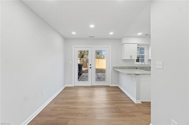 interior space featuring light wood-type flooring, french doors, white cabinetry, and baseboards