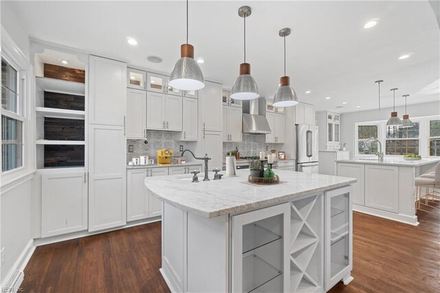 kitchen with a spacious island, white cabinetry, high quality fridge, and wall chimney range hood