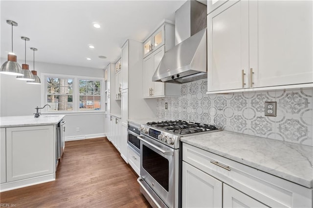 kitchen featuring wall chimney exhaust hood, glass insert cabinets, appliances with stainless steel finishes, light stone counters, and white cabinetry