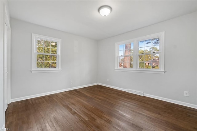 spare room with dark wood finished floors, visible vents, and baseboards