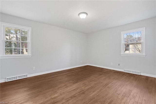 empty room with wood finished floors, visible vents, and baseboards