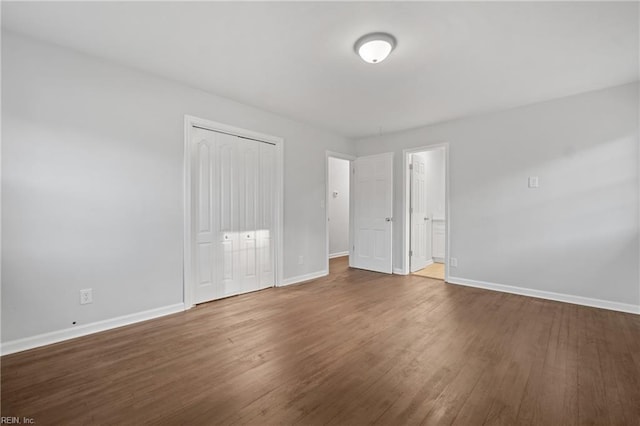unfurnished bedroom featuring dark wood-style flooring, a closet, and baseboards