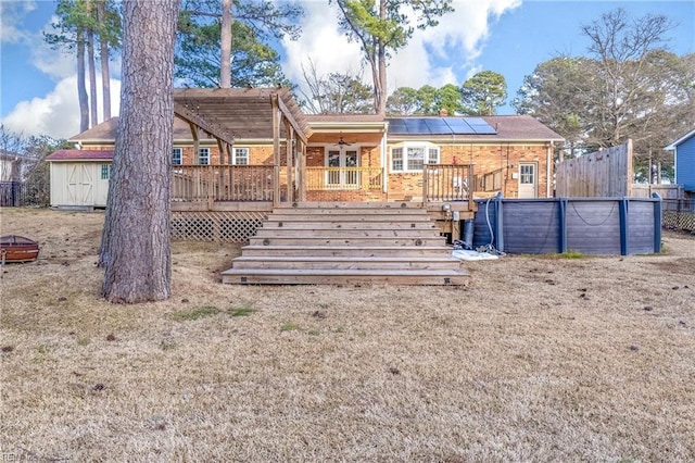 back of property featuring a deck, ceiling fan, solar panels, brick siding, and fence