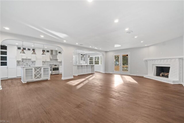 unfurnished living room with dark wood-type flooring, a brick fireplace, a sink, and baseboards