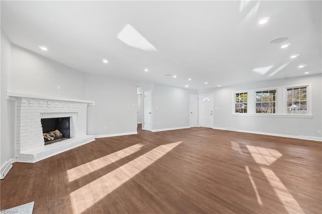 unfurnished living room with recessed lighting, a brick fireplace, baseboards, and wood finished floors