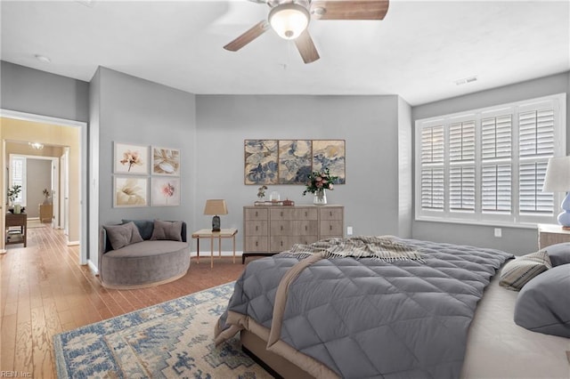 bedroom featuring a ceiling fan, visible vents, baseboards, and wood finished floors