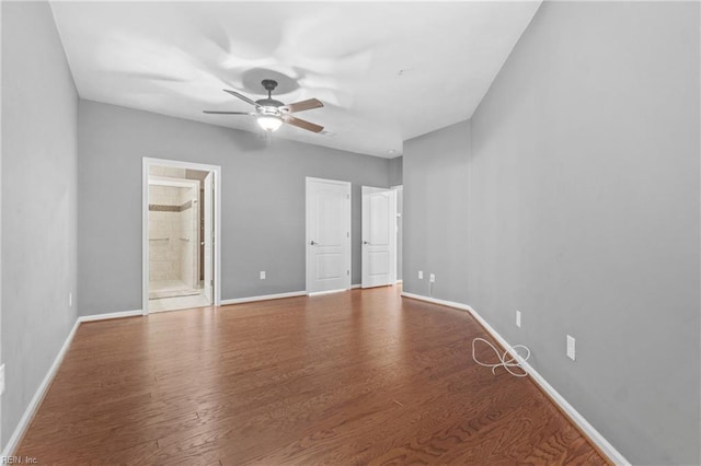 unfurnished bedroom with ensuite bath, wood finished floors, a ceiling fan, and baseboards