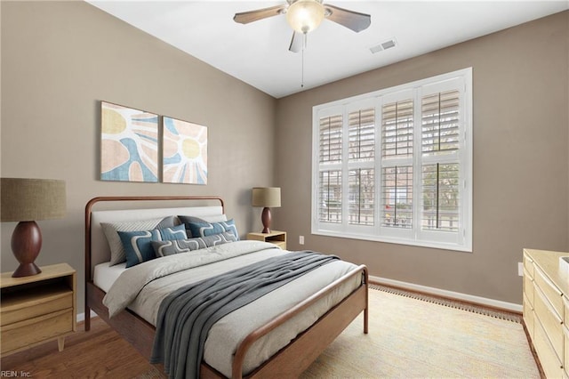 bedroom featuring a ceiling fan, visible vents, baseboards, and wood finished floors