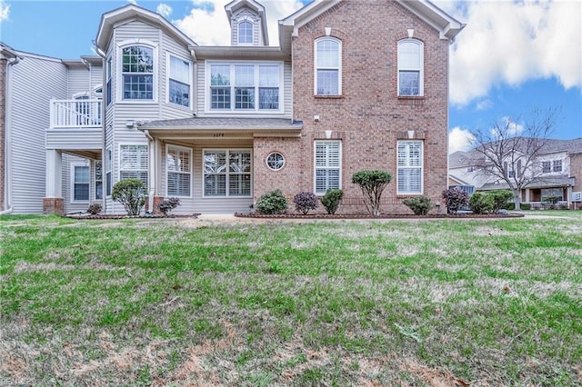 view of front of house with brick siding, a front yard, and a balcony