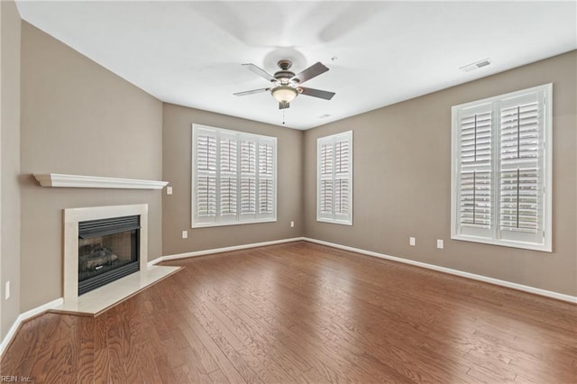 unfurnished living room with wood finished floors, a ceiling fan, visible vents, baseboards, and a glass covered fireplace