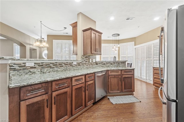 kitchen with a peninsula, appliances with stainless steel finishes, decorative backsplash, and a notable chandelier