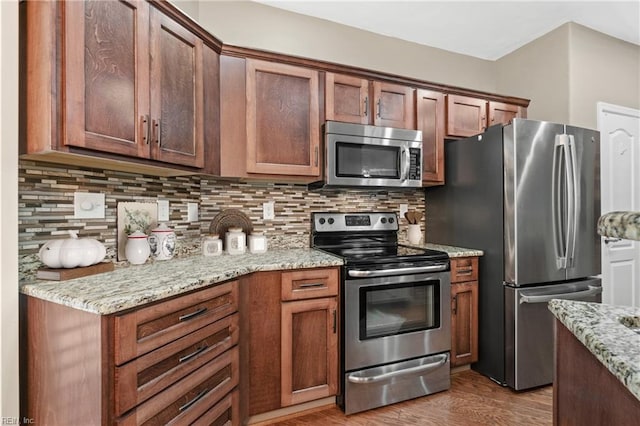 kitchen featuring wood finished floors, appliances with stainless steel finishes, backsplash, and light stone countertops