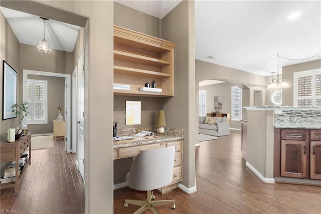 hallway featuring arched walkways, baseboards, and wood finished floors