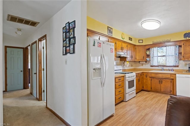 kitchen with white appliances, visible vents, light countertops, under cabinet range hood, and a sink