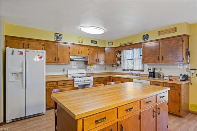 kitchen with light wood-type flooring, white appliances, under cabinet range hood, and a sink