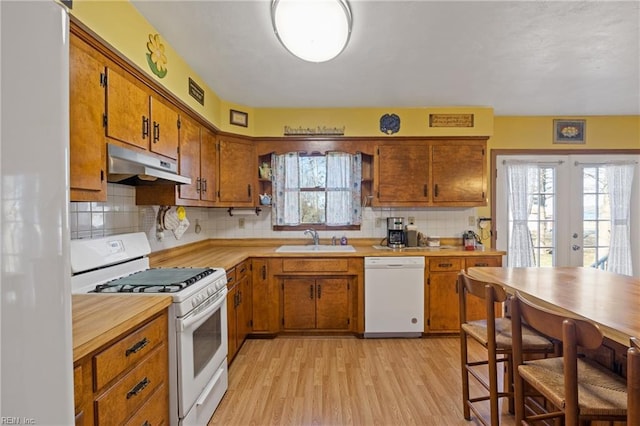 kitchen with white appliances, brown cabinetry, a sink, and under cabinet range hood