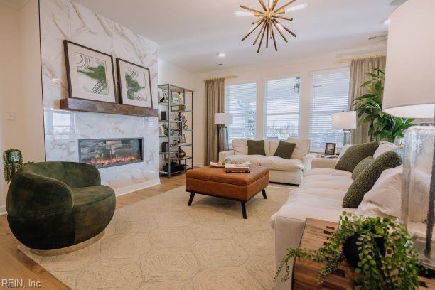 living room with a notable chandelier, ornamental molding, a premium fireplace, and light wood-style floors