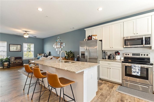 kitchen with white cabinets, an island with sink, light wood-style flooring, stainless steel appliances, and a sink