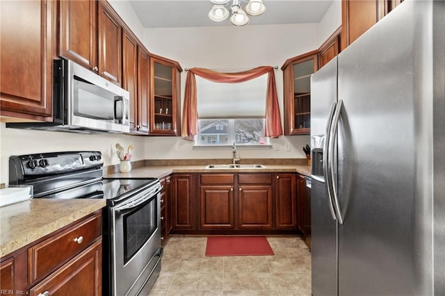 kitchen featuring brown cabinetry, glass insert cabinets, stainless steel appliances, and a sink