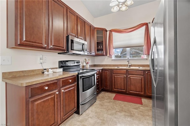 kitchen with a sink, light countertops, appliances with stainless steel finishes, brown cabinetry, and glass insert cabinets