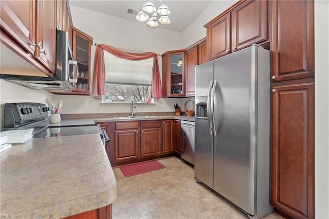 kitchen featuring glass insert cabinets, a sink, stainless steel appliances, light countertops, and a notable chandelier