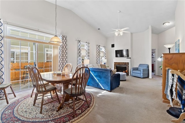 carpeted dining area featuring ceiling fan, high vaulted ceiling, and a fireplace