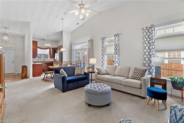 living room featuring ceiling fan with notable chandelier, high vaulted ceiling, a wealth of natural light, and light colored carpet