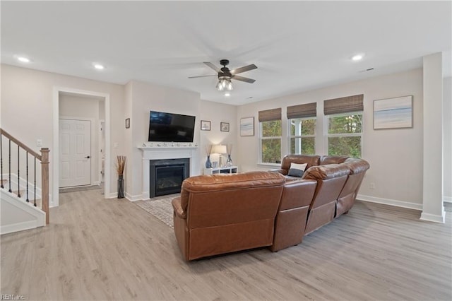 living room with light wood-style flooring, recessed lighting, baseboards, stairway, and a glass covered fireplace