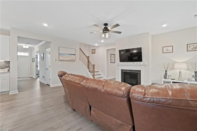 living area featuring light wood-style flooring, recessed lighting, baseboards, stairway, and a glass covered fireplace