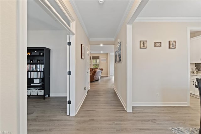 hallway featuring ornamental molding, light wood-type flooring, and baseboards