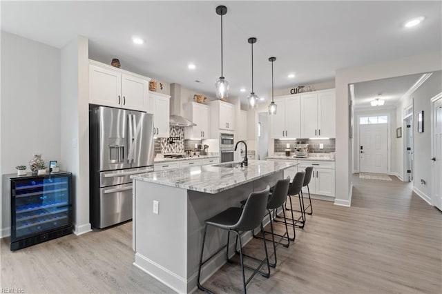 kitchen with appliances with stainless steel finishes, wine cooler, white cabinets, and wall chimney exhaust hood