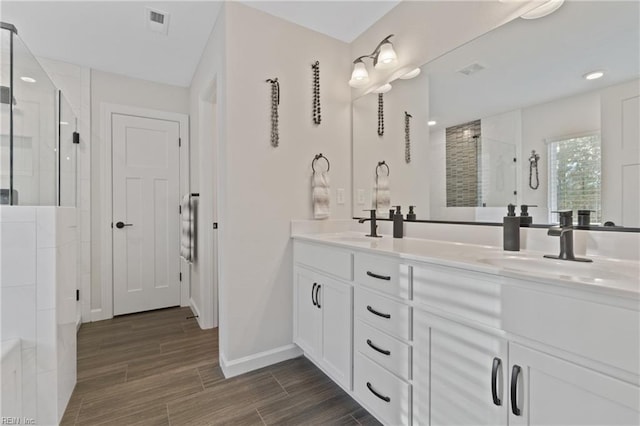 bathroom with double vanity, visible vents, wood tiled floor, a sink, and a shower stall