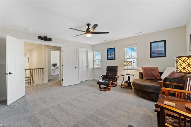 living area with a ceiling fan, carpet, baseboards, and an upstairs landing