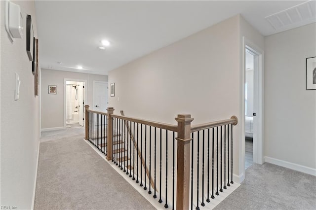 hallway featuring an upstairs landing, baseboards, visible vents, and carpet flooring