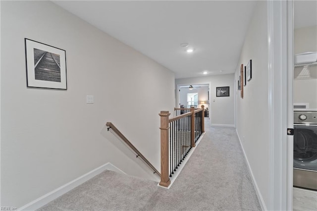 hall featuring baseboards, washer / clothes dryer, an upstairs landing, and light colored carpet