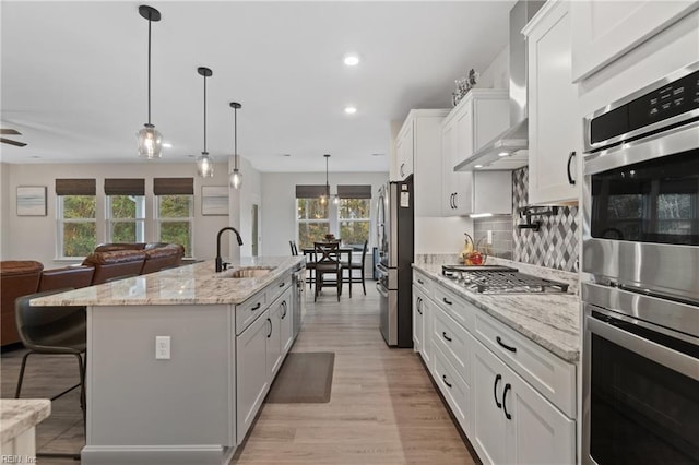 kitchen with stainless steel appliances, a breakfast bar, a sink, open floor plan, and wall chimney exhaust hood