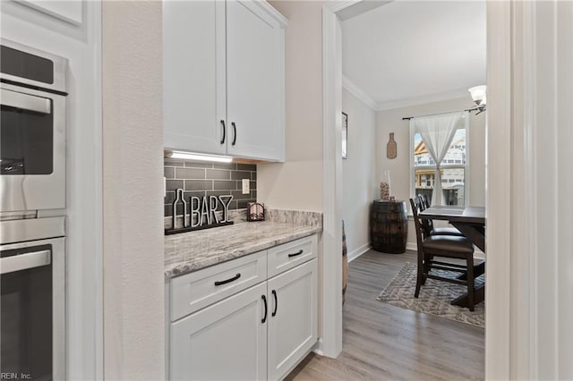 kitchen featuring white cabinetry, baseboards, light wood-style floors, ornamental molding, and decorative backsplash