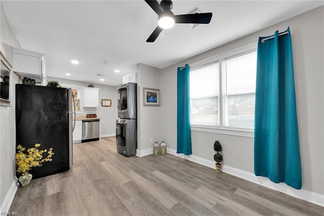 kitchen with stacked washer and clothes dryer, appliances with stainless steel finishes, light wood-style floors, white cabinetry, and baseboards