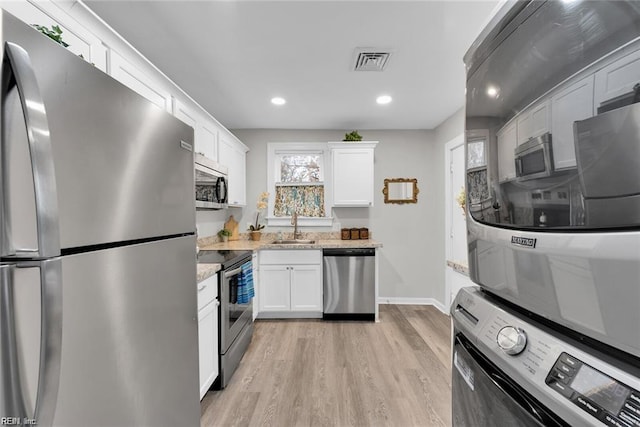 kitchen featuring stacked washer and dryer, visible vents, appliances with stainless steel finishes, white cabinetry, and a sink