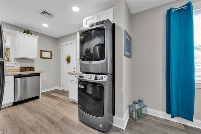 kitchen with white cabinets, baseboards, light wood-style floors, stainless steel dishwasher, and stacked washer and clothes dryer