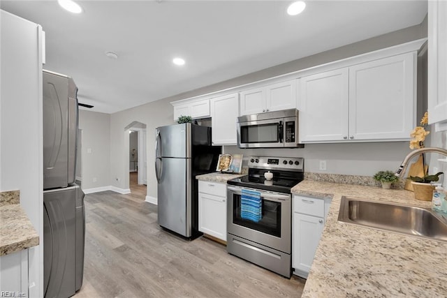 kitchen with appliances with stainless steel finishes, arched walkways, white cabinetry, and a sink