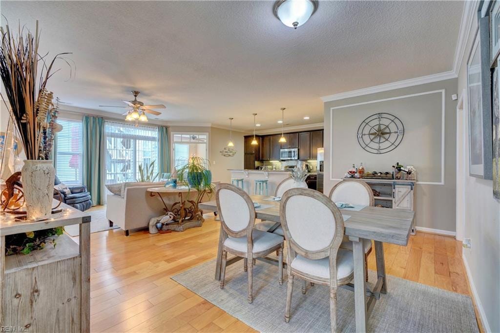 dining area with ornamental molding, light wood-style floors, a textured ceiling, and baseboards